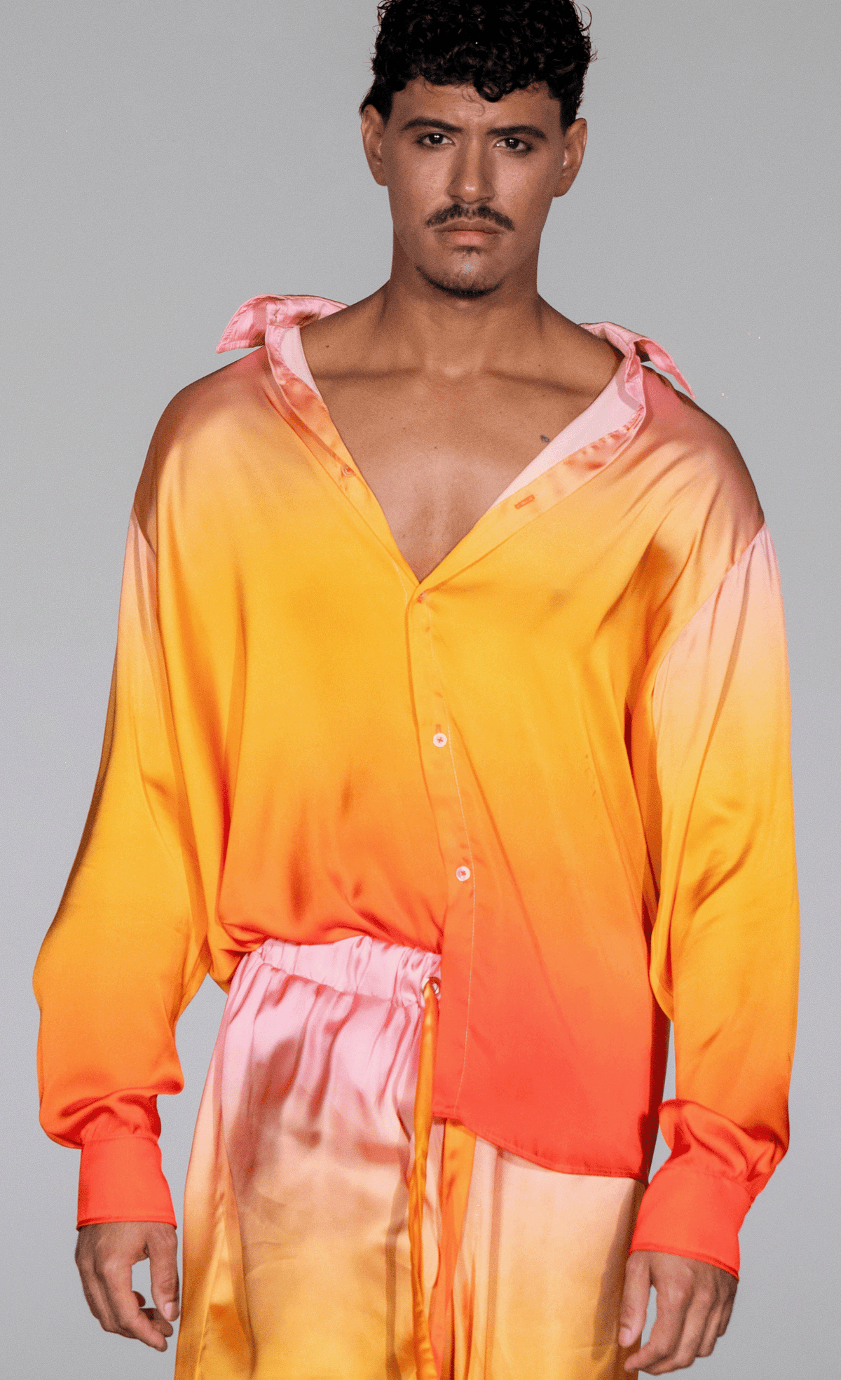 Model wearing a long sleeve ombré button-down shirt in Sundown Ombré (tangerine to neon coral gradient), Stephen Michael Oliver Sol Top.